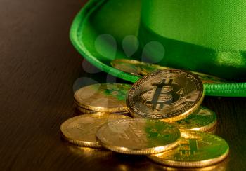 Treasure of golden bitcoins inside a green velvet hat on wooden table to celebrate luck on St Patrick's Day of March 17th