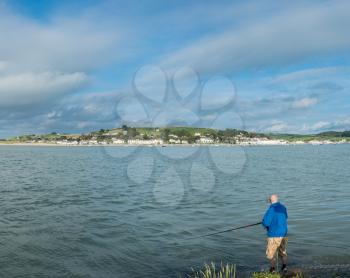 Male angler fishing from the coast in the sea at Appledore in North Devon, UK