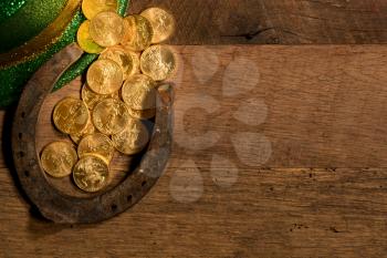 Treasure of pure gold coins from a green hat on rustic wooden table into horseshoe to celebrate luck on St Patrick's Day