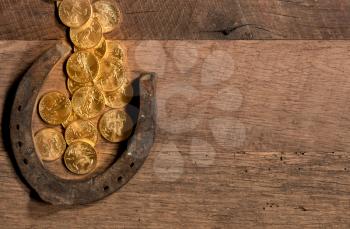 Treasure of pure gold coins flowing on rustic wooden table into horseshoe to celebrate luck on St Patrick's Day