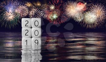 Calendar blocks showing 2019 sinking into the ocean as 2020 starts with fireworks in the background