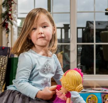Young female toddler girl at Christmas opening presents and gifts and holding a doll