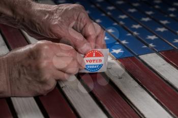 Senior caucasian hand removing sticker of I Voted Today stickers for the US elections with flag in background