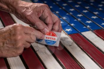 Senior caucasian hand removing sticker of I Voted Today stickers for the US elections with flag in background