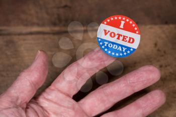 I Voted Today sticker on senior caucasian mans finger on rustic rural wooden table