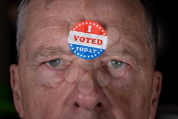 I Voted Today sticker on senior caucasian mans forehead with angry stern stare at camera