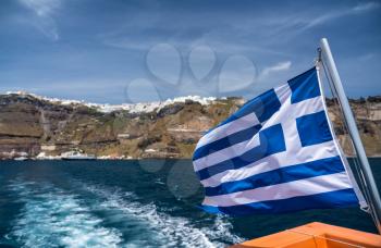 Greek flag on tender boat leaving Fira port on Santorini