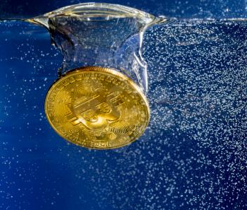Bitcoin coin dropped into water and sinking below bubble to show the falling price of cyber currency