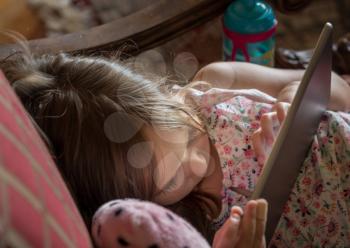Young toddler lying on chair and playing games on an electronic tablet device