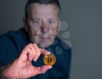 Senior man offering a bitcoin as a bribe or a payment for a ransom or malware