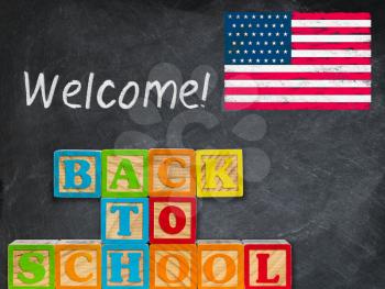 Stack of wooden blocks stacked to spell Back to School against blackboard background with US Flag