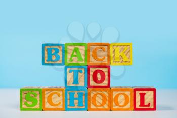 Stack of wooden blocks stacked to spell Back to School against blue background with copy space