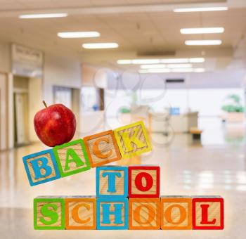 Back to School with wooden blocks with red apple on top. Background is a school entrance or corridor