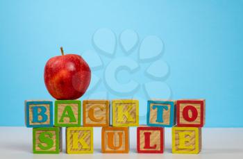 Stack of wooden blocks wrongly spelling Back to School with red apple on top against blue background