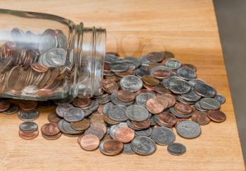 Hundreds of US coins pouring out of savings jar on wooden table as concept for shortage of loose change in USA