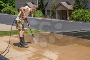 Senior caucasian man spraying concrete driveway with high pressure water spray to clean it