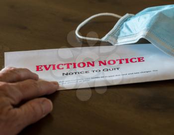 Defaulting renter with facemask receives letter giving notice of eviction from home on wooden table
