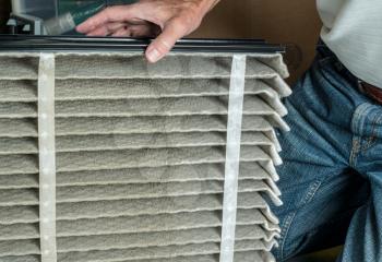 Senior caucasian man looking at the dust in folded dirty air filter in the HVAC furnace system in basement of home