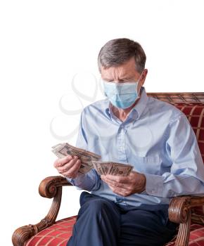 Senior caucasian man counting some US dollar bills. He is wearing face mask to prevent coronavirus. Isolated against white background