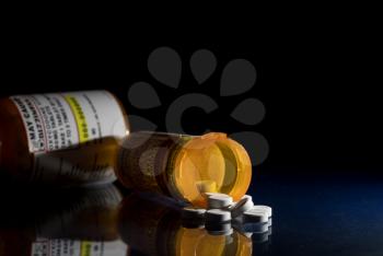 Oxycodone is the generic name for a range of opoid pain killing tablets. Prescription bottle for Oxycodone tablets and pills on glass table with reflections