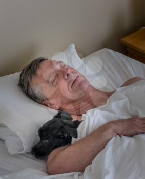 Senior retired man asleep in bed and snuggling his pet terrier dog. Could be used as illustration of importance of pets to older people