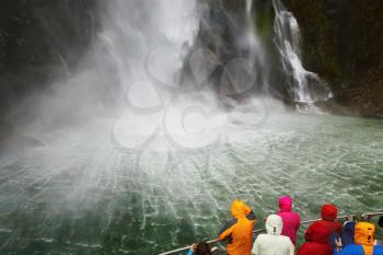 People on the boat near spectacular waterfall, Milford Sound fiord, New Zealand
