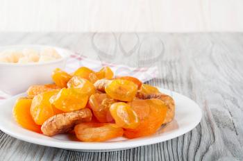 Dried fruits in white plate on a wooden background. Lemons, apricots and figs. 