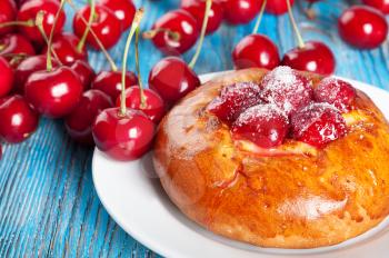 Fresh homemade bun with sweet cherry in a white dish on a blue wooden background