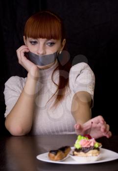 The girl, whose mouth sealed with tape extends at plate with cakes