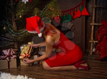 Young sexy girl in a bright red dress is considering in the dark room gifts under the Christmas tree