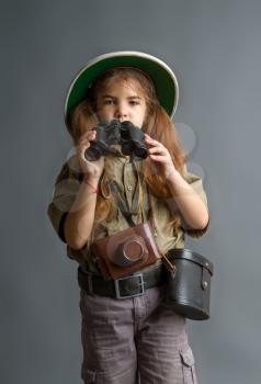 a little girl in a tropical khaki uniform and a cork helmet looks over her binoculars