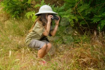 a little girl in a tropical khaki uniform and a cork with binoculars looking for adventures in nature