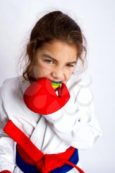 A little karate girl in white kimono and in a red and blue belt at the same time puts on her mouth guard in preparation for the fight.