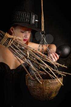 sexy girl dressed as a medieval witch with a broom in her hand conjures over a cauldron