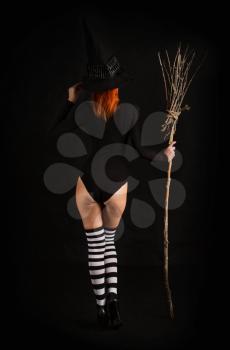 sexy girl dressed as a medieval witch stands with a broom in her hands