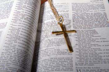 Open holy bible close up and a small metal cross on a chain