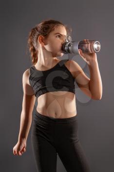 little tired girl in sportswear drinks water and rests after a workout on a dark background