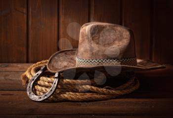 An old horseshoe lies next to a classic cowboy hat and lasso on a dark wooden background.