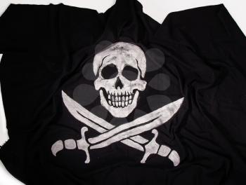 traditional waving pirate flag jolly roger skull with two crossed sabers on dark fabric background