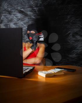 young girl in a sexy red dress and a balaclava mask sits at a laptop and makes an honest profit on the Internet