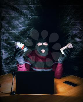 a bandit in a mask of a balaclava using a laptop does not fair profit on the Internet
