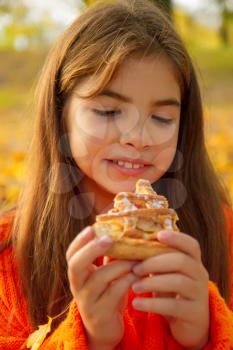 little girl in a bright orange sweater on a picnic in nature eats a delicious homemade cake