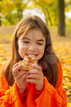 little girl in a bright orange sweater on a picnic in nature eats a delicious homemade cake