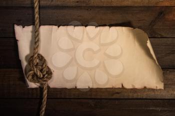 old sheet of parchment or paper lying on wooden boards and a coarse rope pulled into a nautical knot forming a frame
