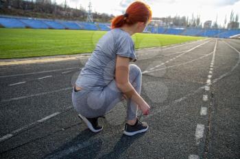young girl getting ready for a run through the stadium and tying shoelaces on sports shoes