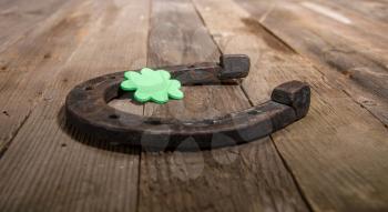 A sheet of artificial clover lies on a real steel horseshoe on a wooden surface