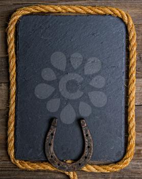 Black chalk board with horseshoe and lasso on wooden background