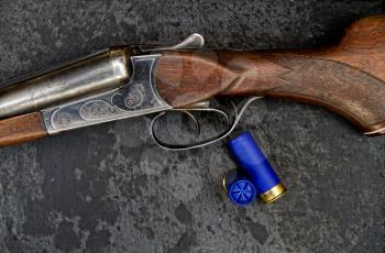 Old classic double-barreled hunting rifle of the twelfth caliber and cartridges for it on a dark background close-up