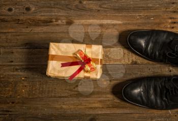 Conceptual photo - a gift wrapped with his own hand by a child for Father's Day next to rough men's shoes on a wooden floor.