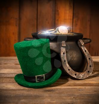 Treasure in a black pot and a green leprechaun hat on a wooden table next to a horseshoe symbol of good luck